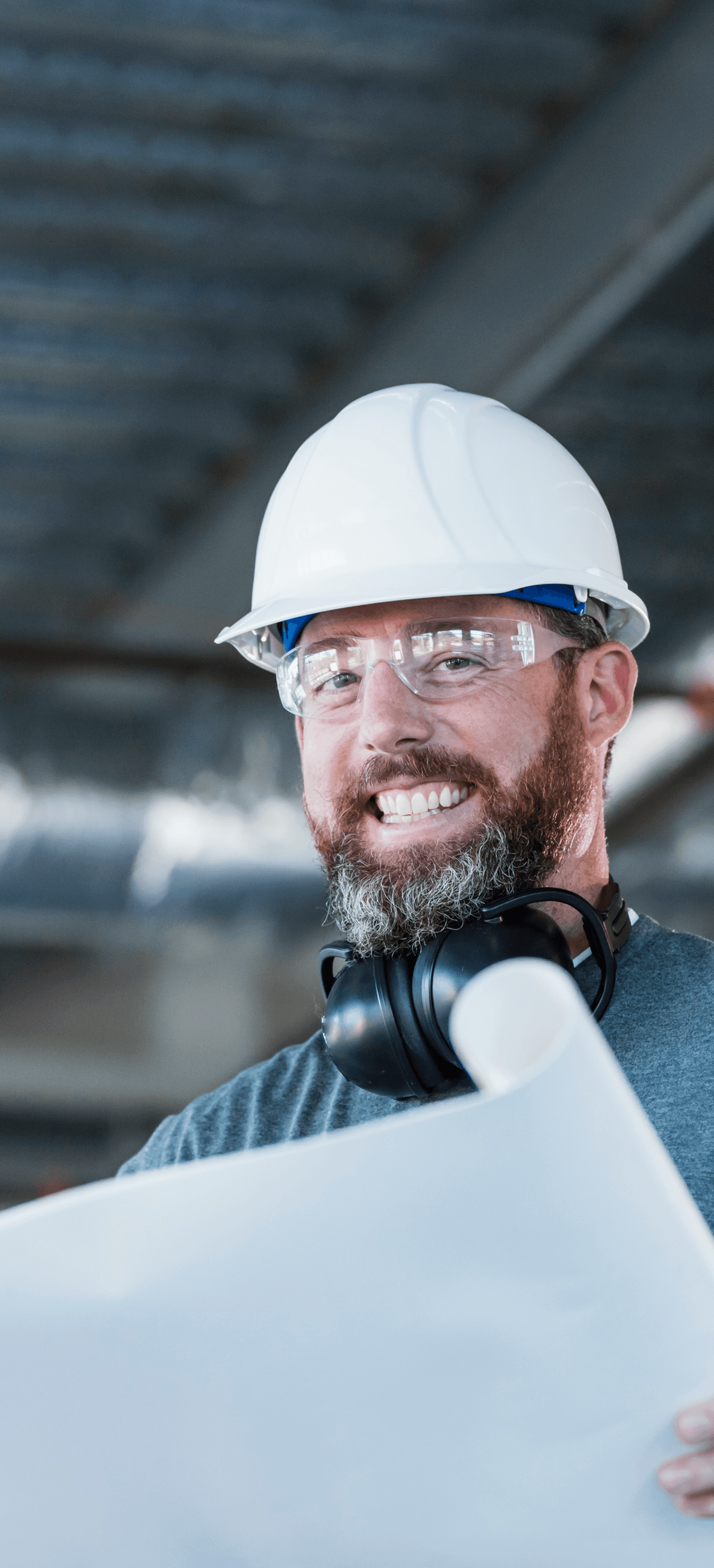 A man wearing safety helmet and holding an open project plan.