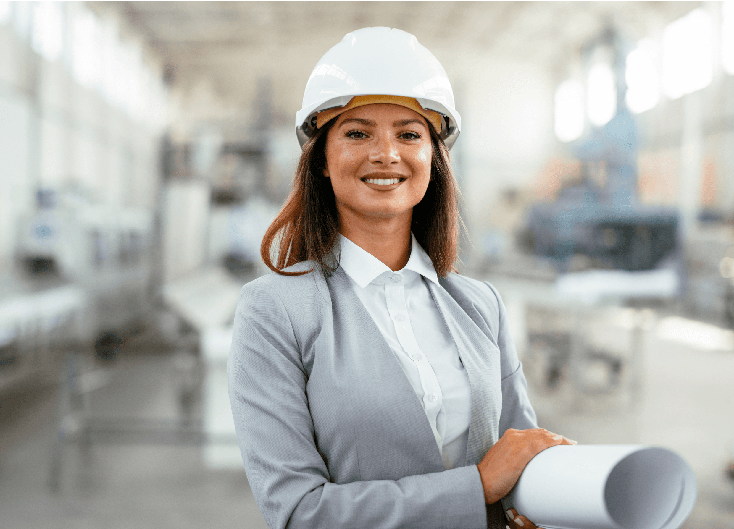 A woman wearing light grey suit and safety helmet is holding a rolled up project plan and smiling.