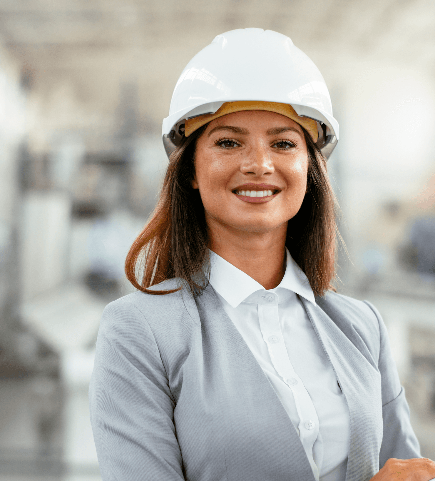 A woman wearing light grey suit and safety helmet is holding a rolled up project plan and smiling.